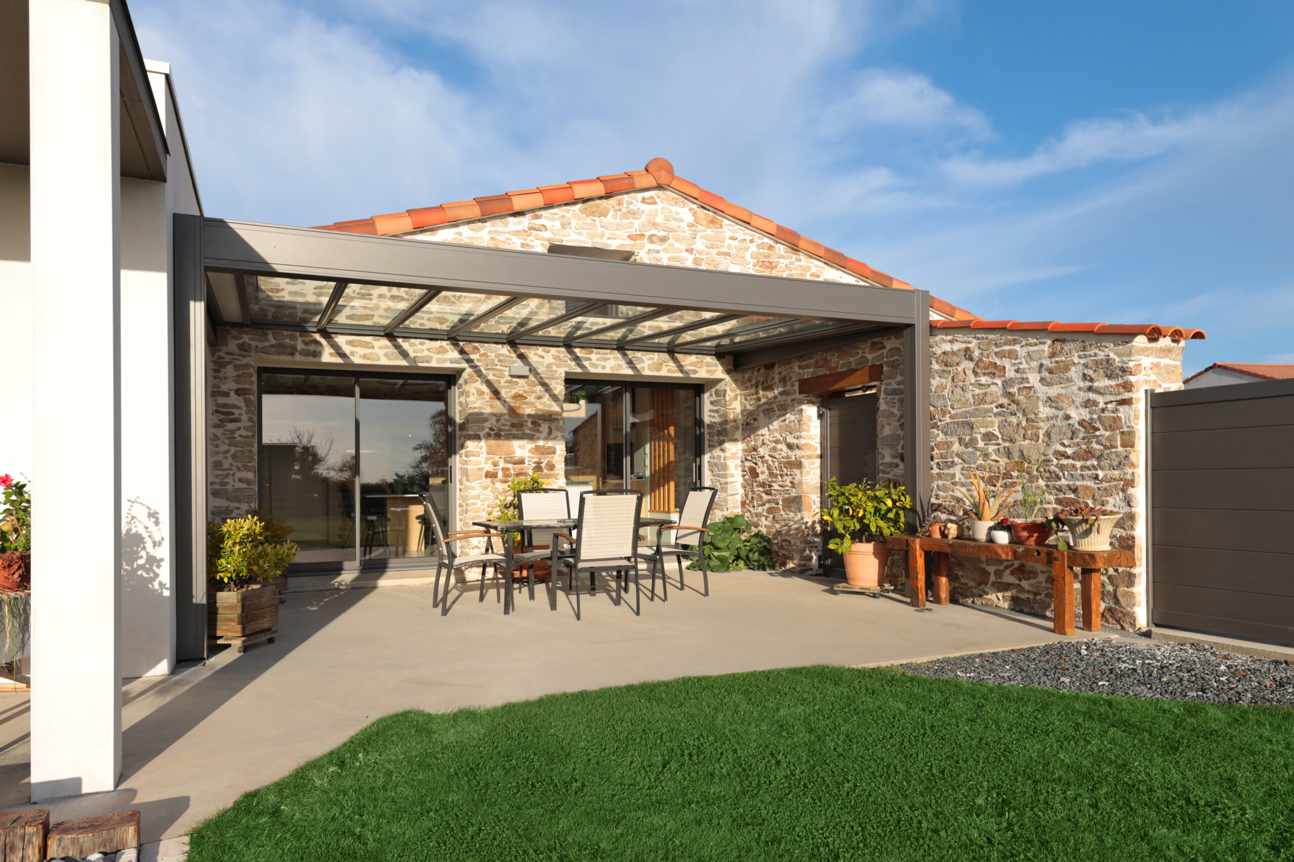 Pergola en aluminium taupe sur terrasse en bois et jardin verdoyant