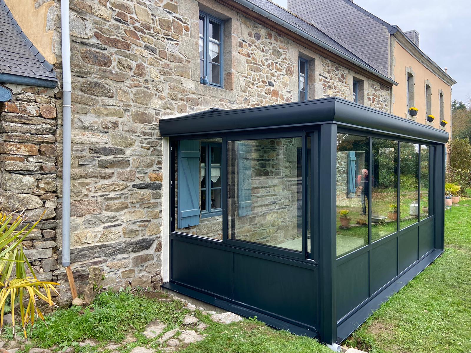 Véranda anthracite installée sur une maison en pierre bretonne